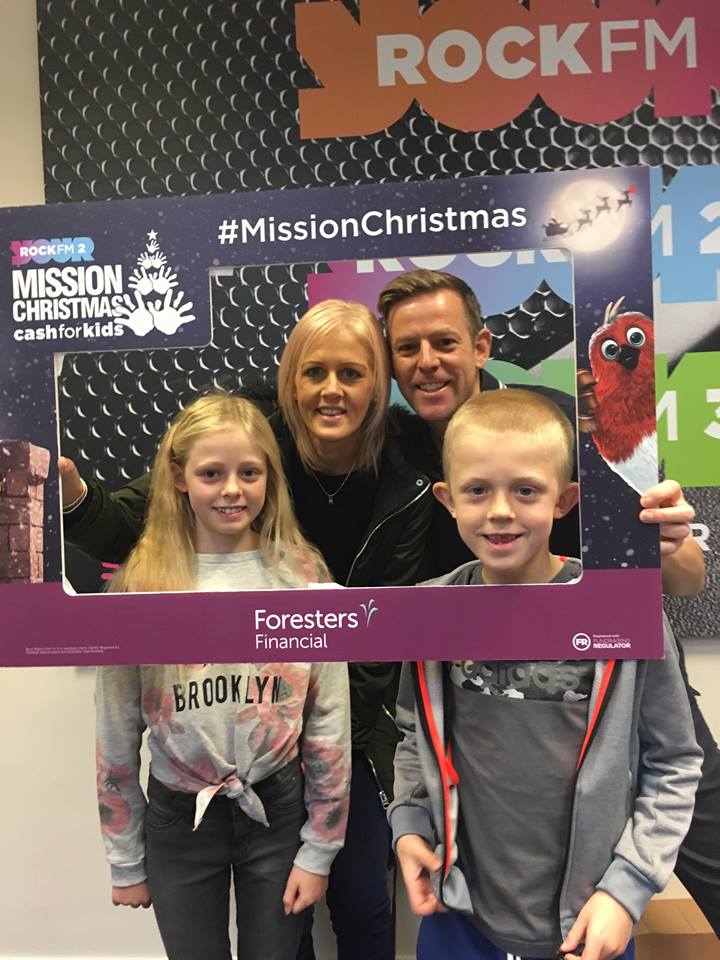 Radio presenters posing with two young children inside a cardboard picture frame promoting Foresters Financial and Mission Christmas