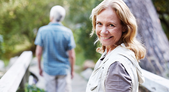 Woman smiling towards camera while man walks across bridge