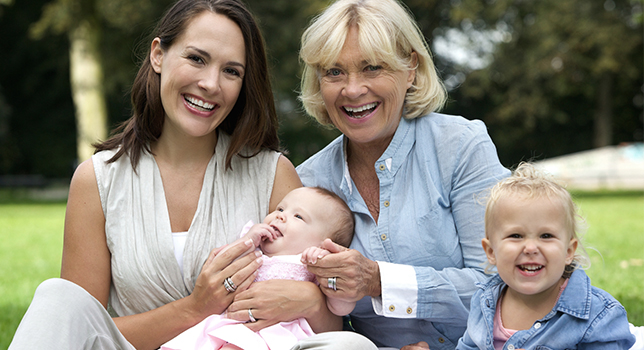 Mother and grandmother sitting on grass holding two babies 